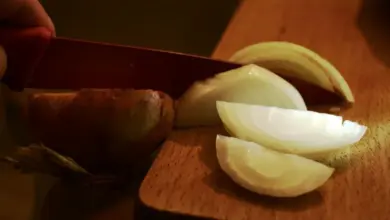 Ruce řezou cibuli na dřevěném prkénku.