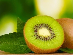 Čerstvé řezané zelené kiwi s listem na dřevěném povrchu.