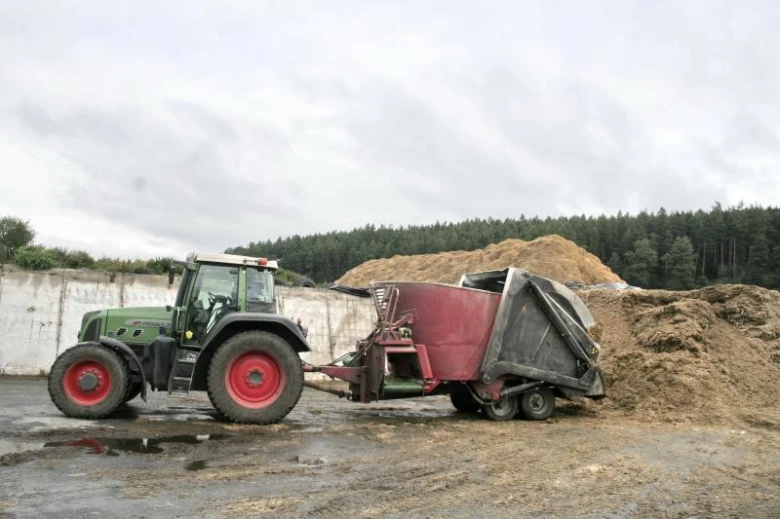 Traktor sklízí kukuřici na poli s vozem plným úrody.