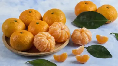 Mandarine v dřevěné misce s listy na modrém pozadí.