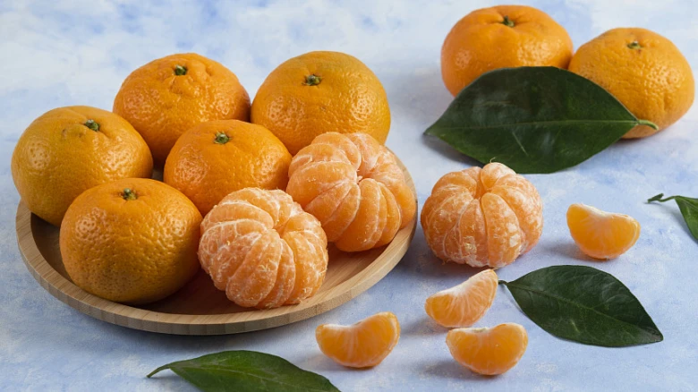 Mandarine v dřevěné misce s listy na modrém pozadí.