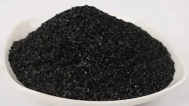 Černé granulované hnojivo v bílé míse na světlém pozadí.