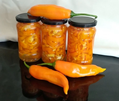 Sklenice s nakládanými oranžovými feferonkami a čerstvé plody.