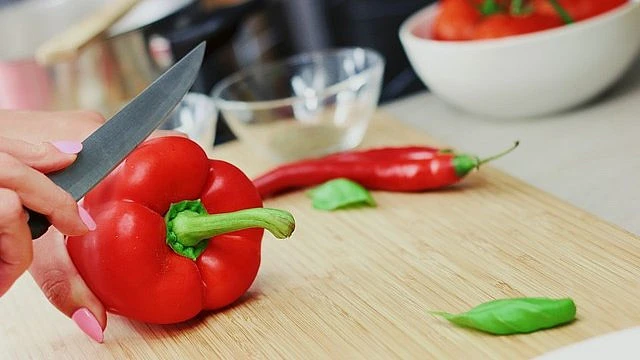 Ruce řezou červenou papriku na dřevěném prkénku.