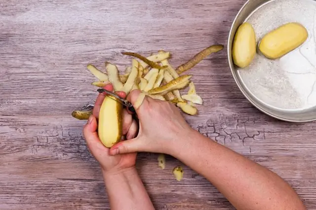 Ruční škrabání bramborových slupek na dřevěném povrchu