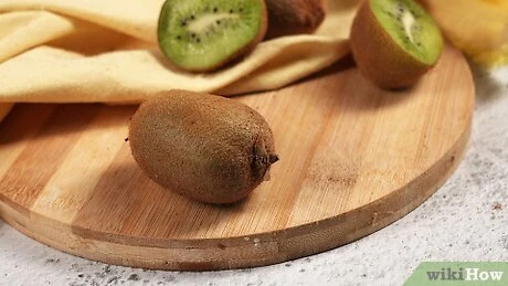 Celé a nakrájené kiwi na dřevěném prkénku.