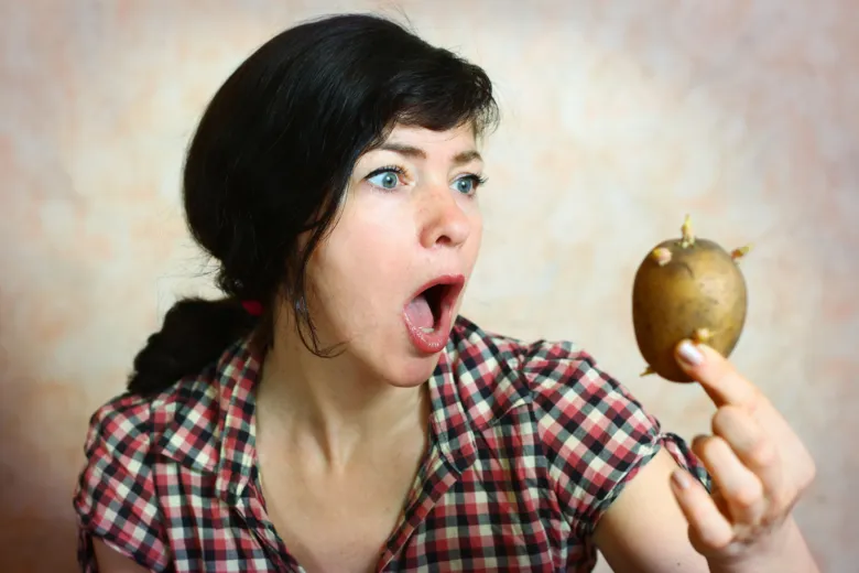 Žena drží starou bramboru s výhonky.