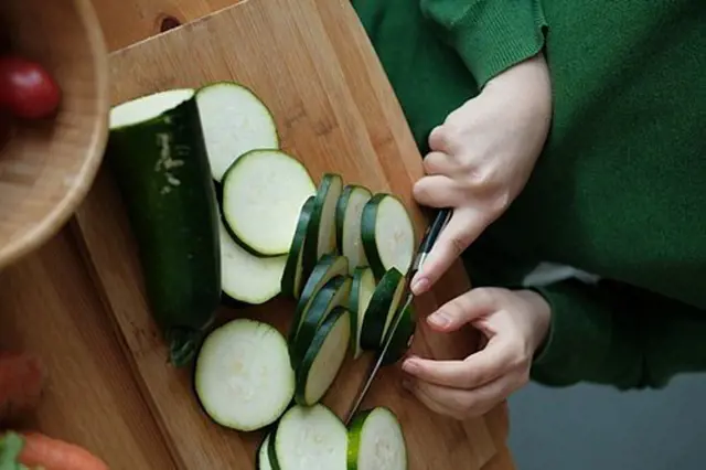Člověk krájí cuketu na dřevěném prknu s nůžkami.