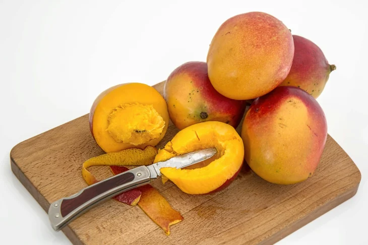 Mango na dřevěném prknu s nožem, jeden nakrájený.