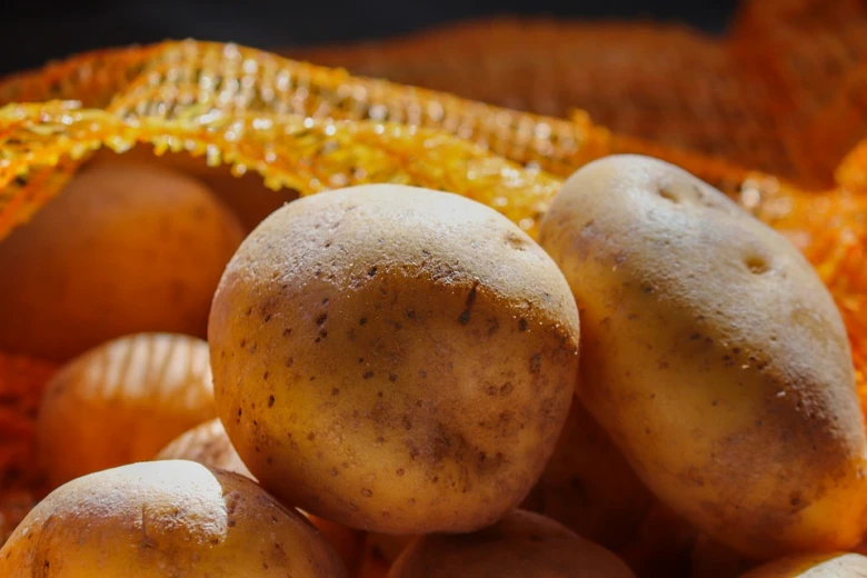 Čerstvé brambory v oranžovém síťovaném pytlíku.