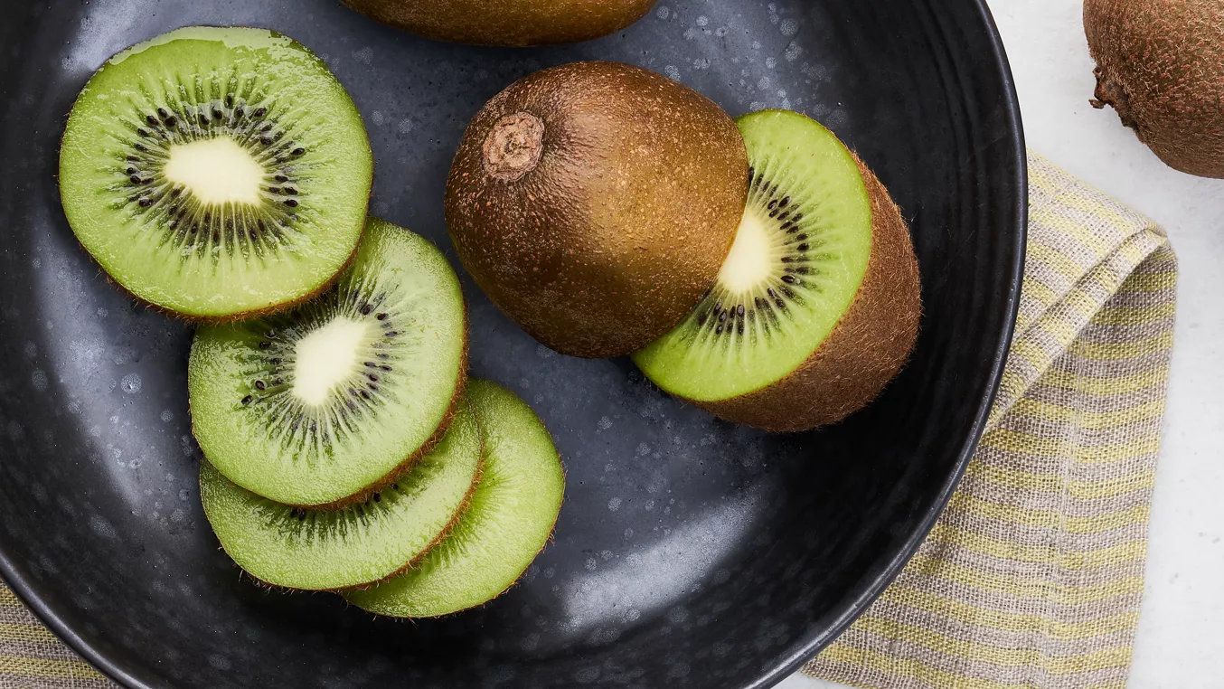 Svěžé nakrájené zelené kiwi na tmavém talíři.