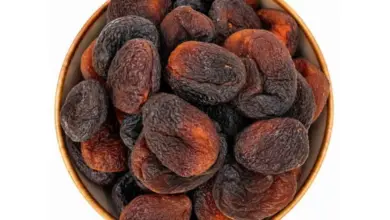 Sušené meruňky v dřevěné mísce na bílém pozadí.