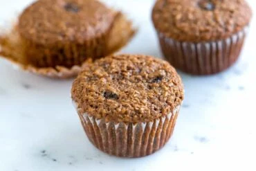 Tři celozrnné muffiny s otrubami na bílém povrchu.