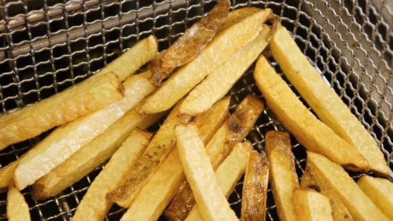 Zlaté hranolky v koši fritézy po vytažení z oleje.