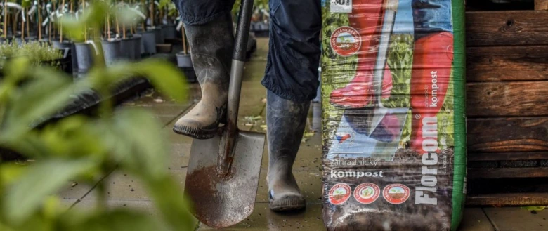 Zahrádkář s lopatou u balíčku kompostu mezi rostlinami.
