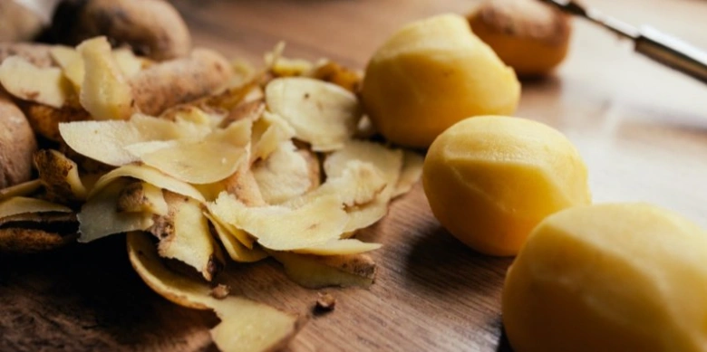 Odloupané žluté brambory s kůrkami na dřevěném povrchu.