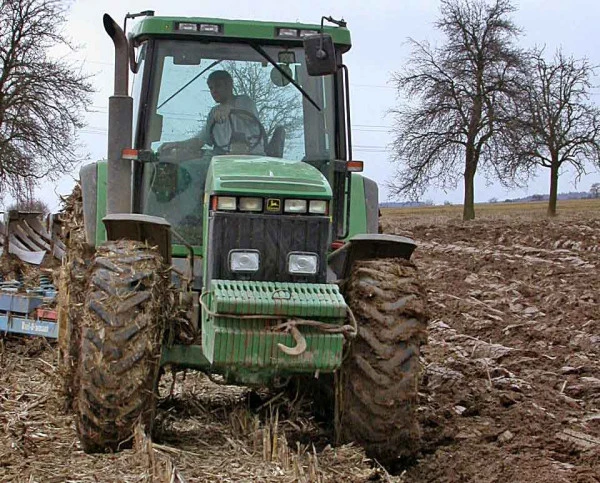 Zelený traktor oruje vlhkou půdu v poli.