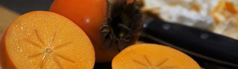 Krájené zralé kaki s viditelnou dužinou a celým ovocem v pozadí.