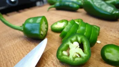 Čerstvé zelené papriky jalapeño se řezají na dřevěném prknu.