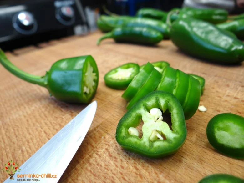 Čerstvé zelené papriky jalapeño se řezají na dřevěném prknu.