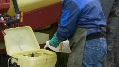 Muž nalévá tekutinu do postřikovače zemědělské techniky.