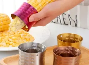 Ruce používají nástroj na loupaní kukuřice ze zrna.