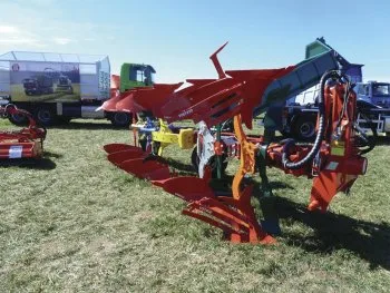 Červený zemědělský pluh na trávnatém pozadí venku