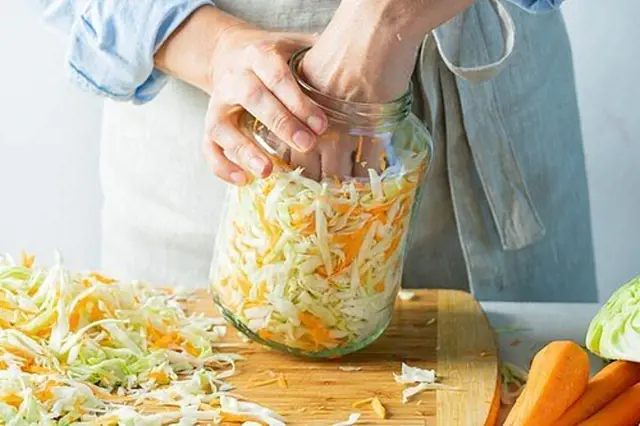 Osobní ruce plnící nakrájené zelí do sklenice na fermentaci.