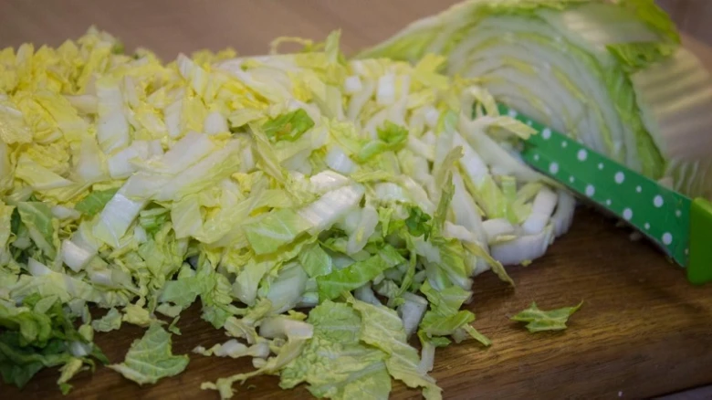 Nakrájené pekingské zelí na dřevěném prknu s nožem