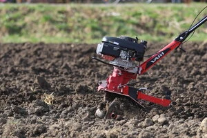 Červený traktor připravuje půdu pro pěstování brambor.