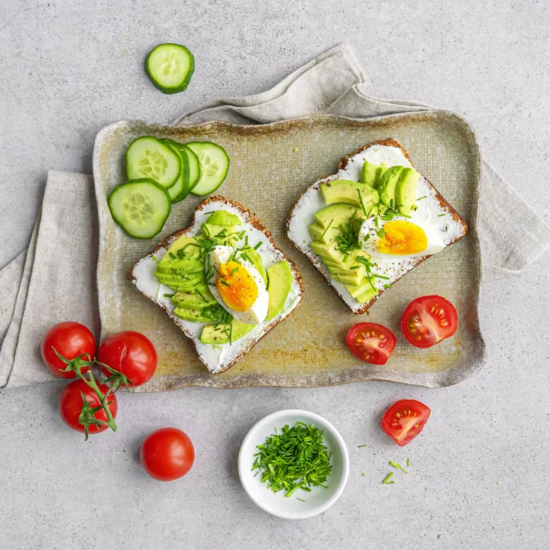 Dva toast s avokádem, vejcem a rajčaty na talíři.